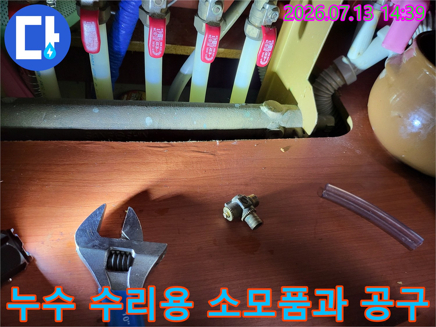 금속제-T형-연결부속과-투명한-호스-그리고-파란색-몽키스패너가-함께-있는-사진