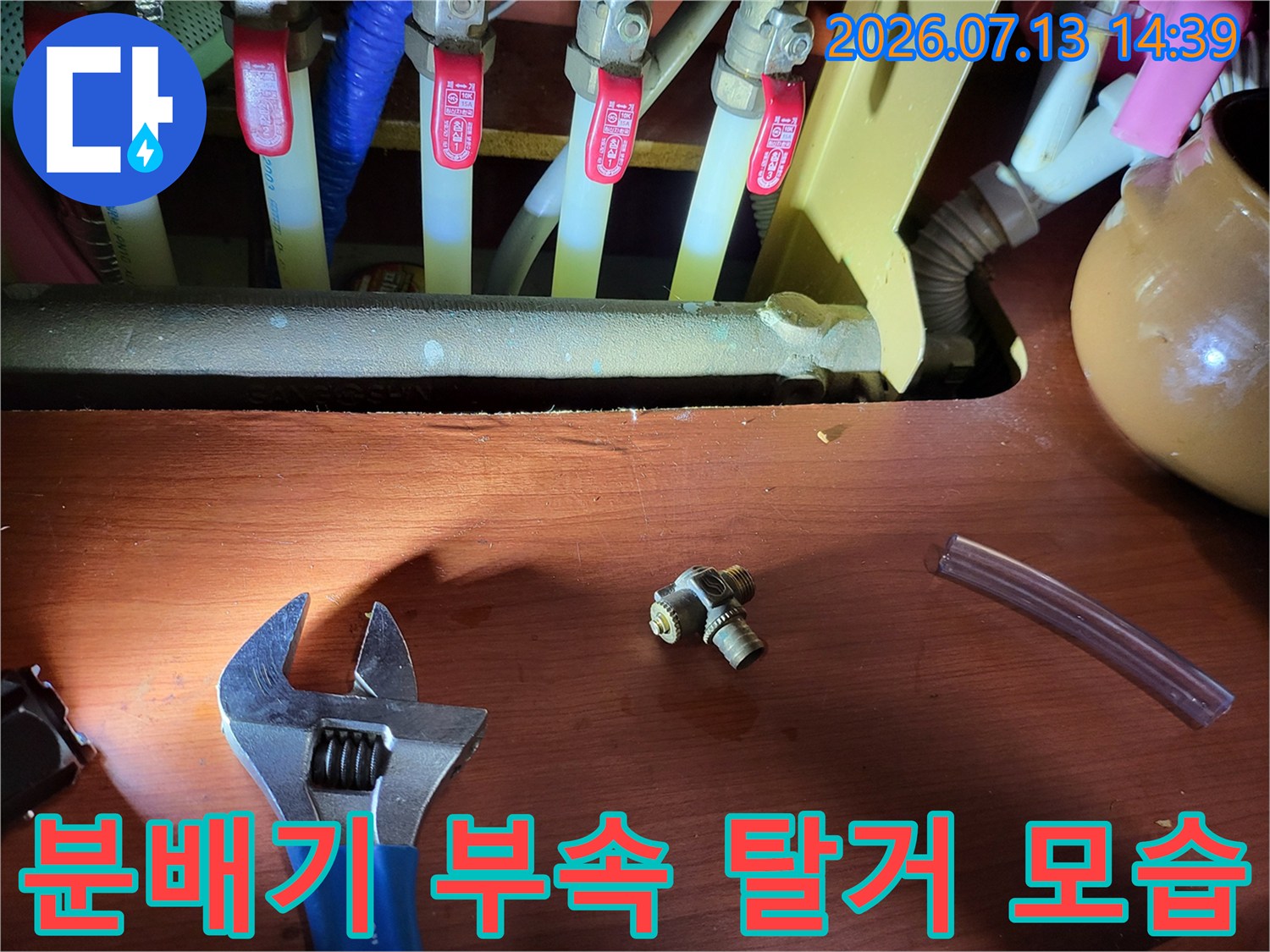 누수가 발생한 분배기의 황동색 티자 연결 부품과 몽키스패너가 놓인 사진