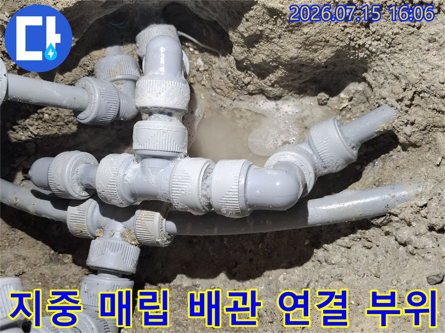 흙 속에 매립된 회색 플라스틱 수도 배관과 여러 개의 연결 부속-부품들