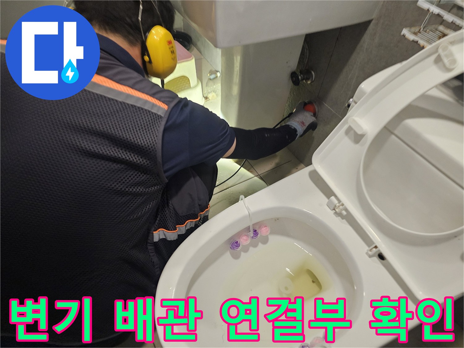 엔지니어가 변기 뒤쪽의 배관 부속 상태를 면밀하게 조사하고 있습니다.