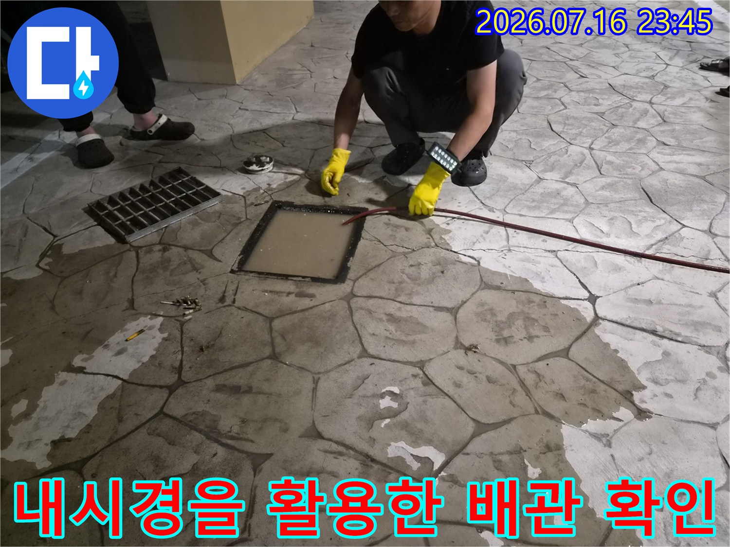 노란 장갑을 낀 작업자가 배수구 안쪽을 내시경으로 정밀하게 살피고 있는 모습