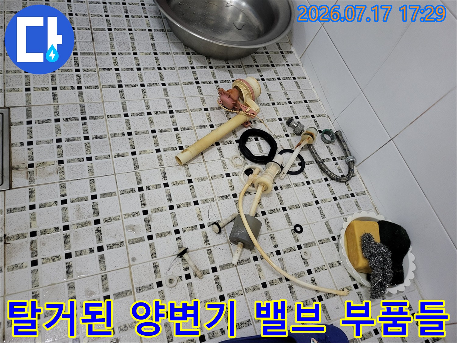 흰색 타일 바닥 위에-양변기 필밸브와 연결 호스 및 세척용 스펀지가 놓여 있는 모습