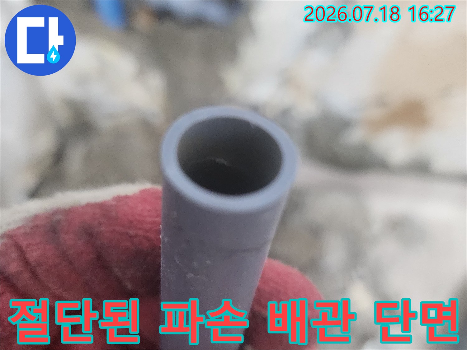 작업자가 장갑을 낀 손으로 절단하여 꺼낸 회색빛의 수도 배관 단면-사진
