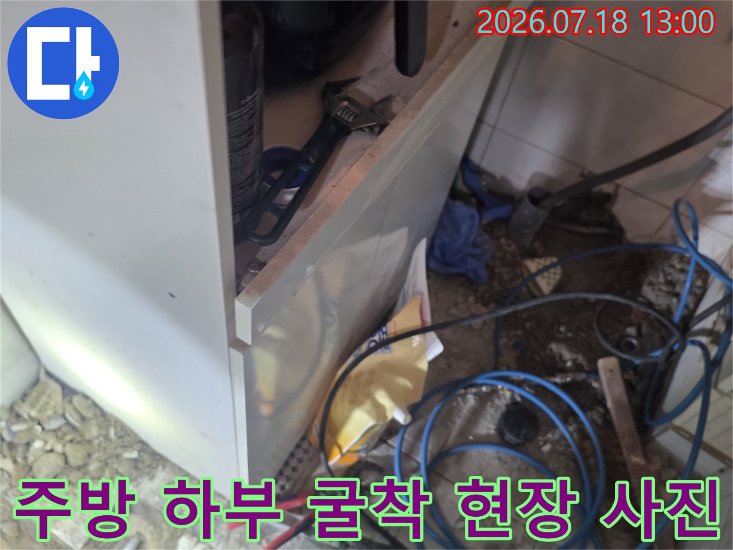 싱크대 아래 바닥면이 파헤쳐져 있으며 파란색 배관과 작업용 장비들이 놓여 있는 모습