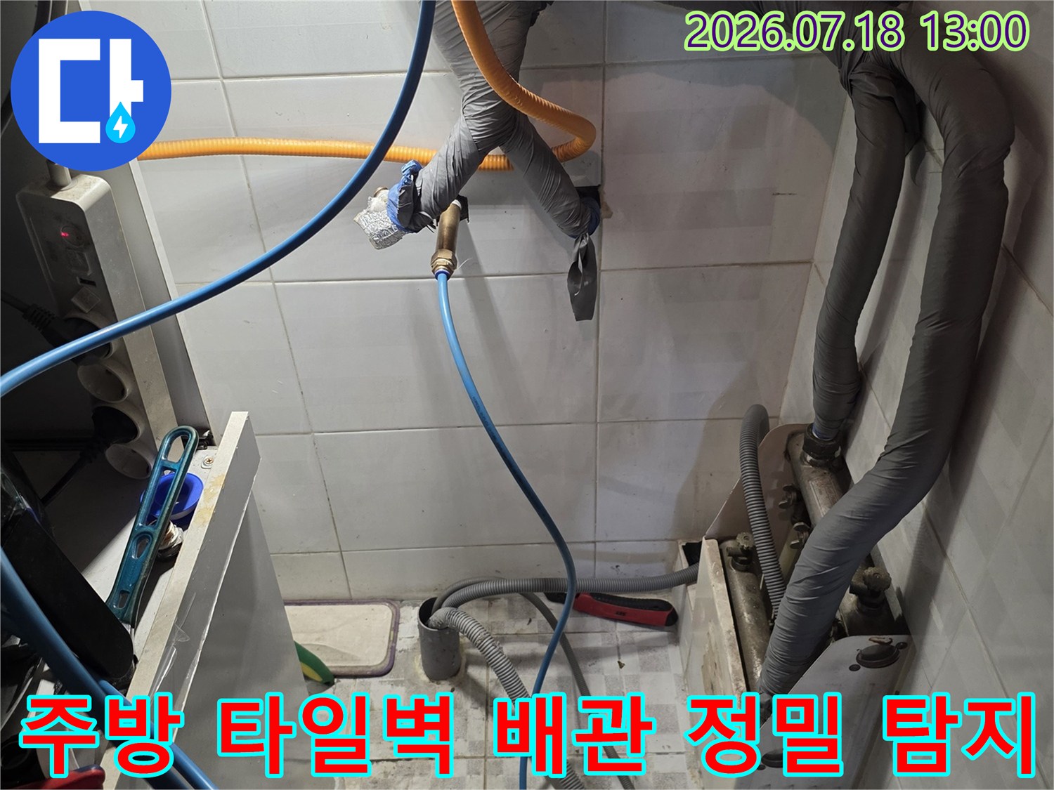 회색 보온재가 씌워진 주방 배관들과 하단에 연결된 파란색 및 노란색 측정용 호스-누수 탐지 중
