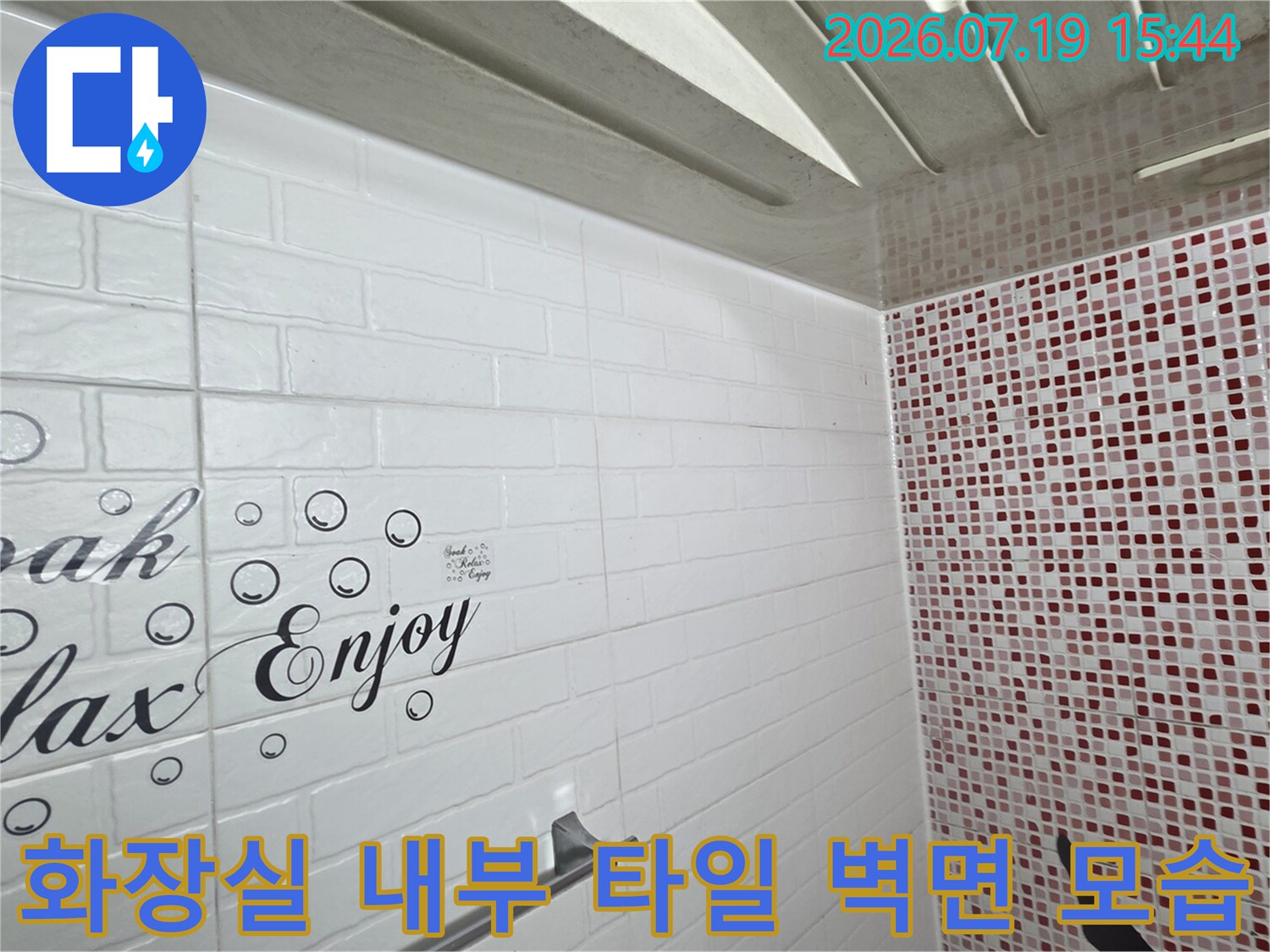 흰색 가로형 타일에 영어 문구가 적혀 있고 붉은색 모자이크 타일이 배치된 욕조 공간 사진