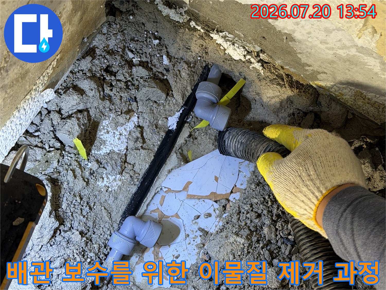 노란색 장갑을 낀 작업자가 진공 흡입기로 배관 주변의 콘크리트 파편을 청소하는 장면