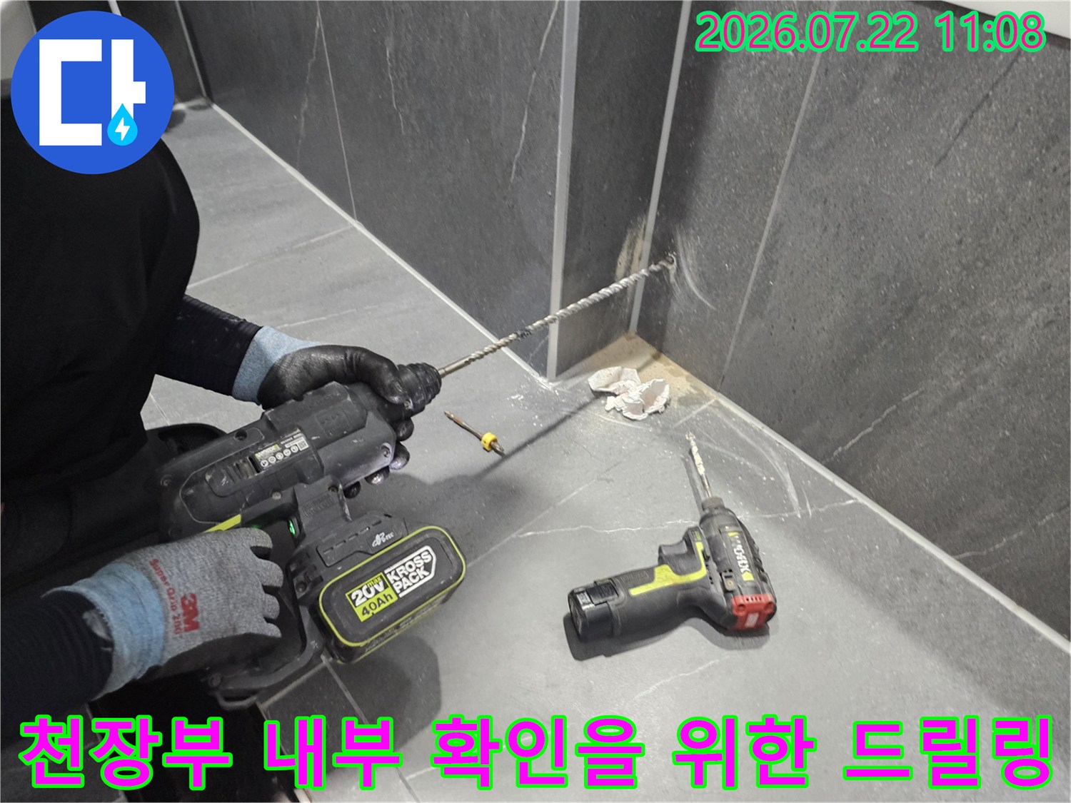 검은색 전동 드릴을 사용하여 회색 천장의 특정 지점을 타공하고 있는 엔지니어의 작업 모습