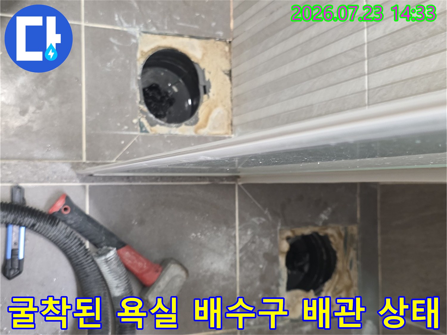 화장실 타일을 제거하고 드러난 두 개의 검은색 배수구 배관과 주변 작업 도구들