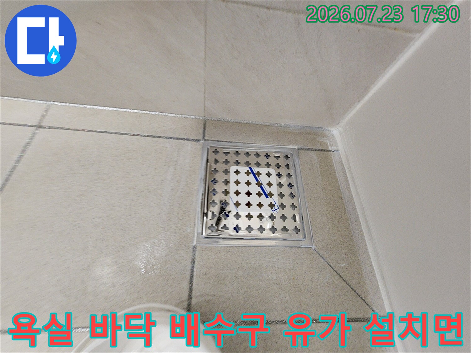 회색빛 타일 마감재와 맞닿아 있는-스테인리스 소재의 욕실 배수구