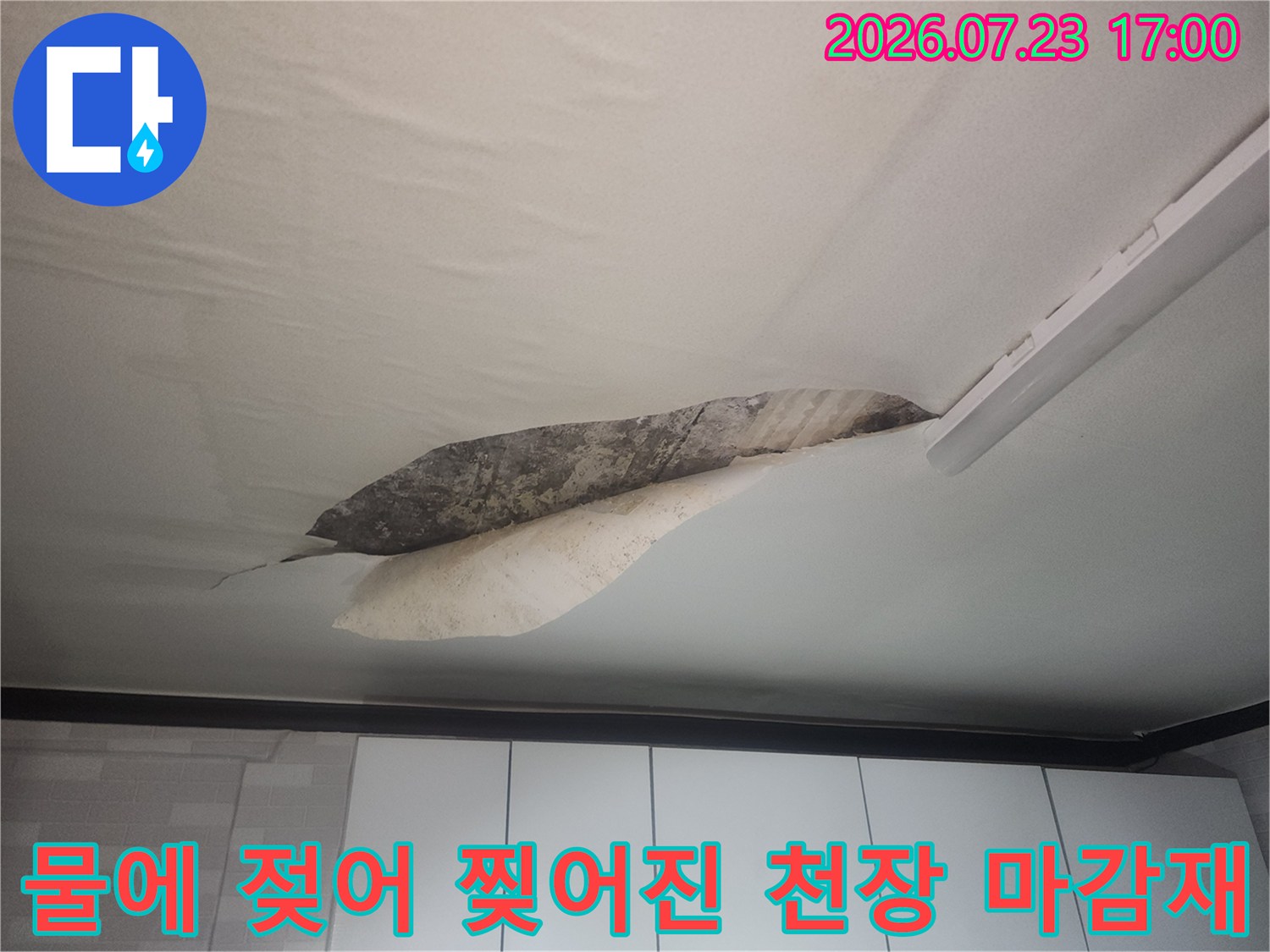물에 젖어 일부가 뜯겨 나가고 내부에 어두운 얼룩이 보이는 거실 천장의 모습