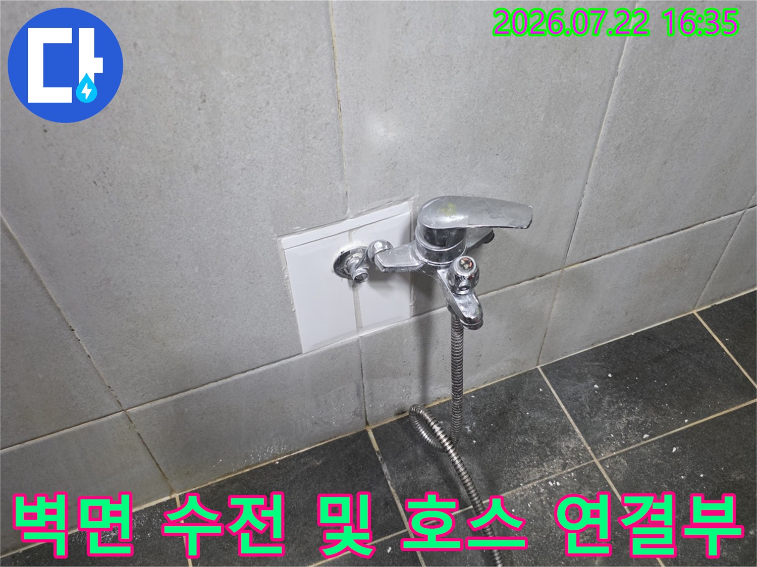 타일 마감재 위에 고정된 금속제 수전과 아래로 내려오는 은색 호스