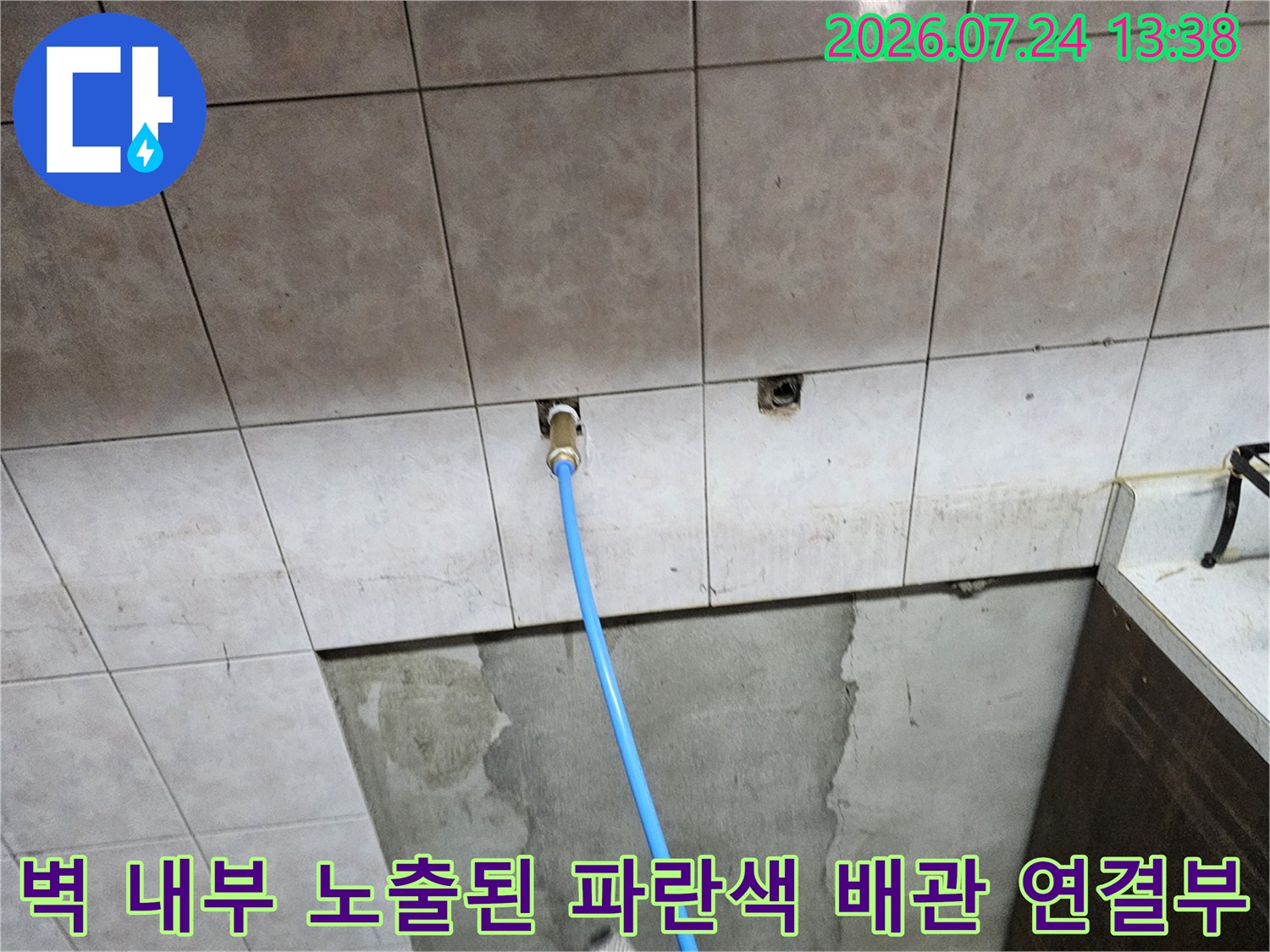 베이지톤 타일 벽면의 굴착 지점에 설치된 파란색 수도 배관과 부속품 사진