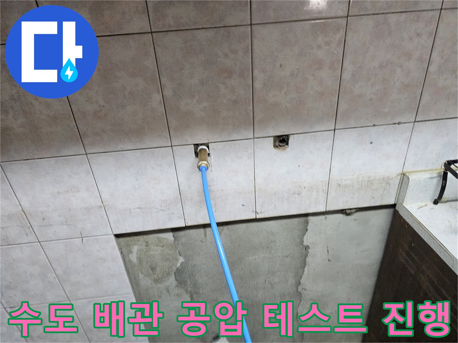 벽면 타일 사이 배관에 연결된 파란색 점검 호스