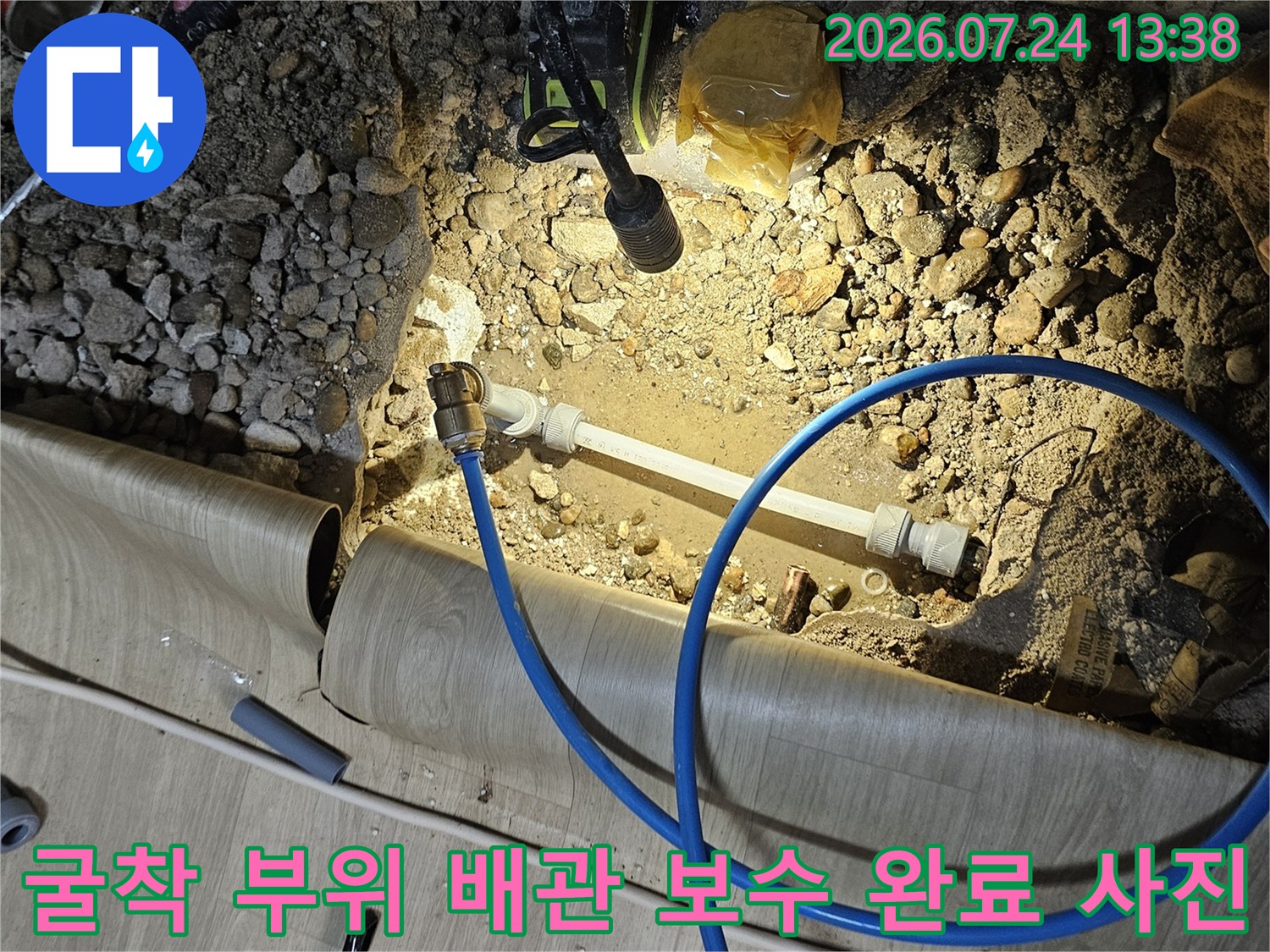 흙과 자갈이 섞인 바닥면 위에 설치된 신규 배관과 파란색 압력 체크 호스