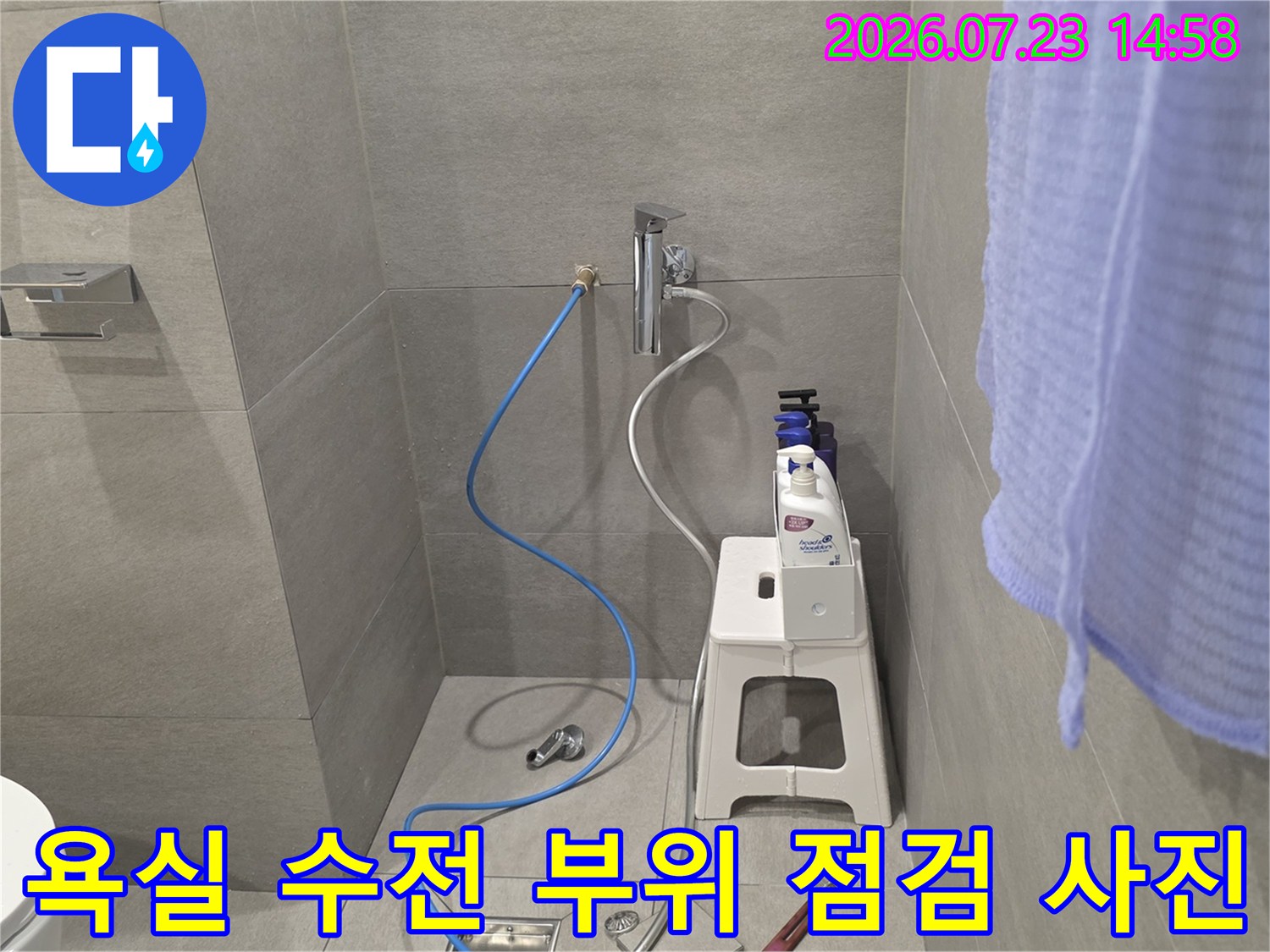 흰색 타일 벽면의 수도꼭지와 연결된 파란색 호스-주변 공구 배치 모습