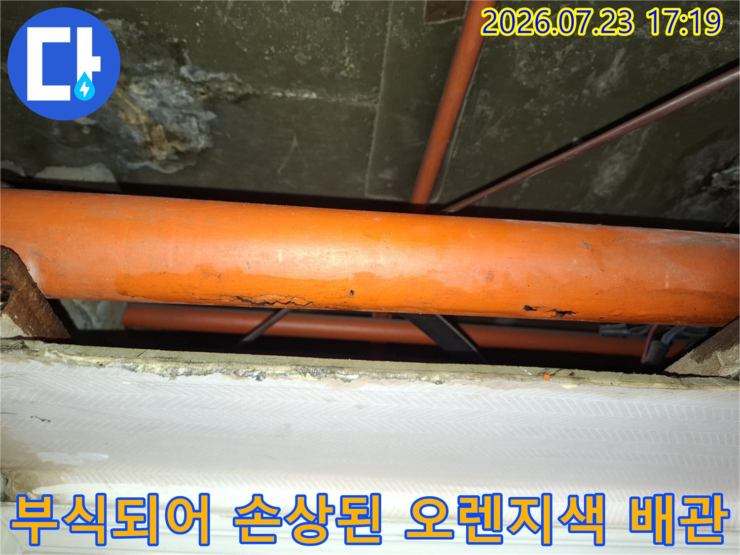천장 내부에 설치된 오렌지색 배관의 표면이 부식되어 껍질이 벗겨진 모습