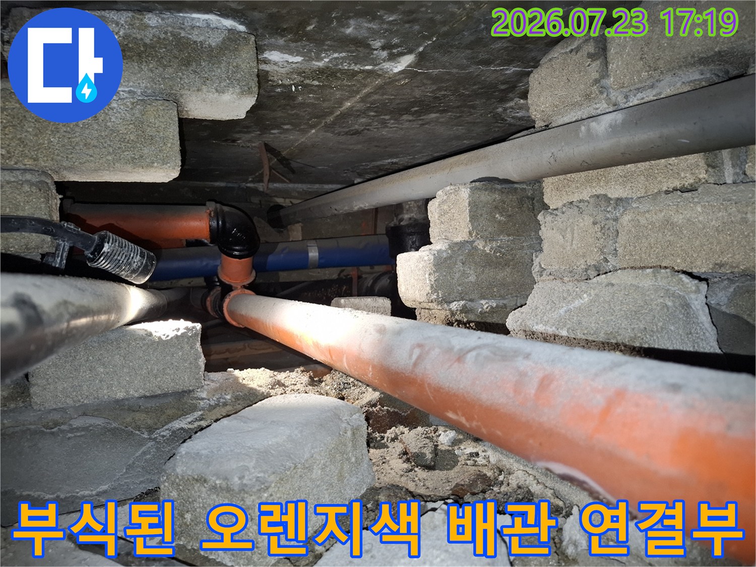 콘크리트-벽돌-사이로-노출된-오렌지색-배관의-연결-엘보우-부분