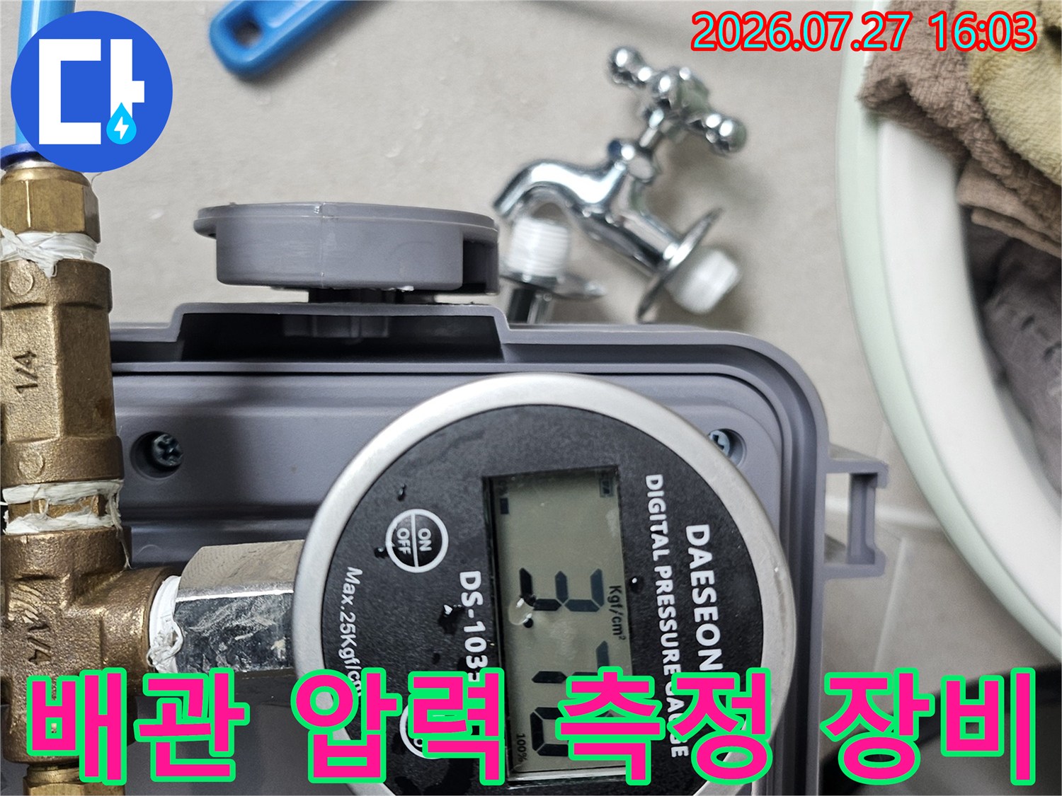 금속 밸브와 파란색 호스가 연결된 디지털 압력 측정기의 클로즈업 사진