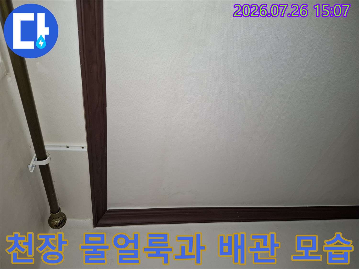 거실 천장의 갈색 몰딩 주변으로 번진 물 얼룩과 금속 배관-고정 장치 사진