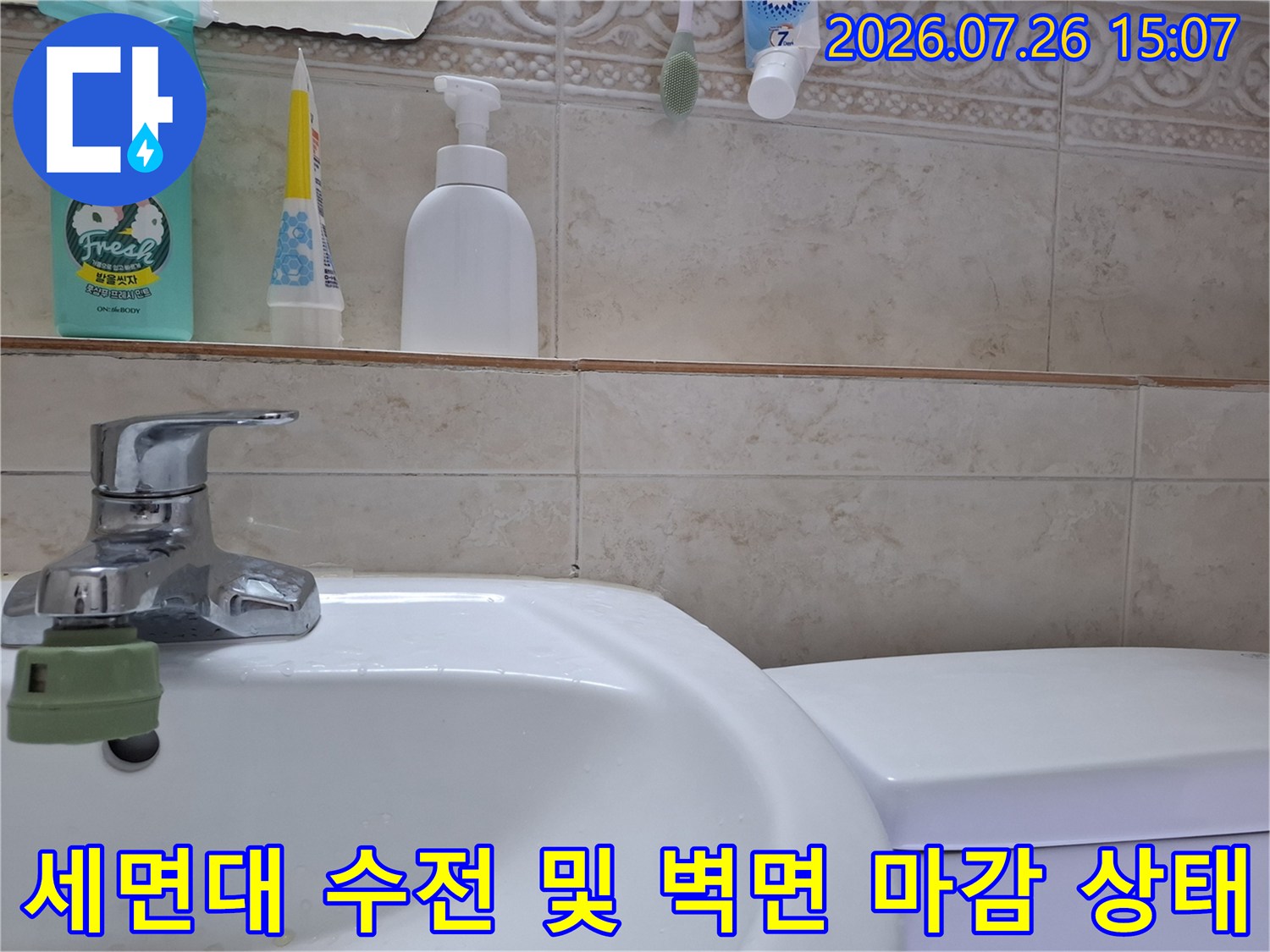 흰색 세면대 위에 설치된 크롬 도금 수전-뒤쪽 베이지색 타일 벽면과 선반