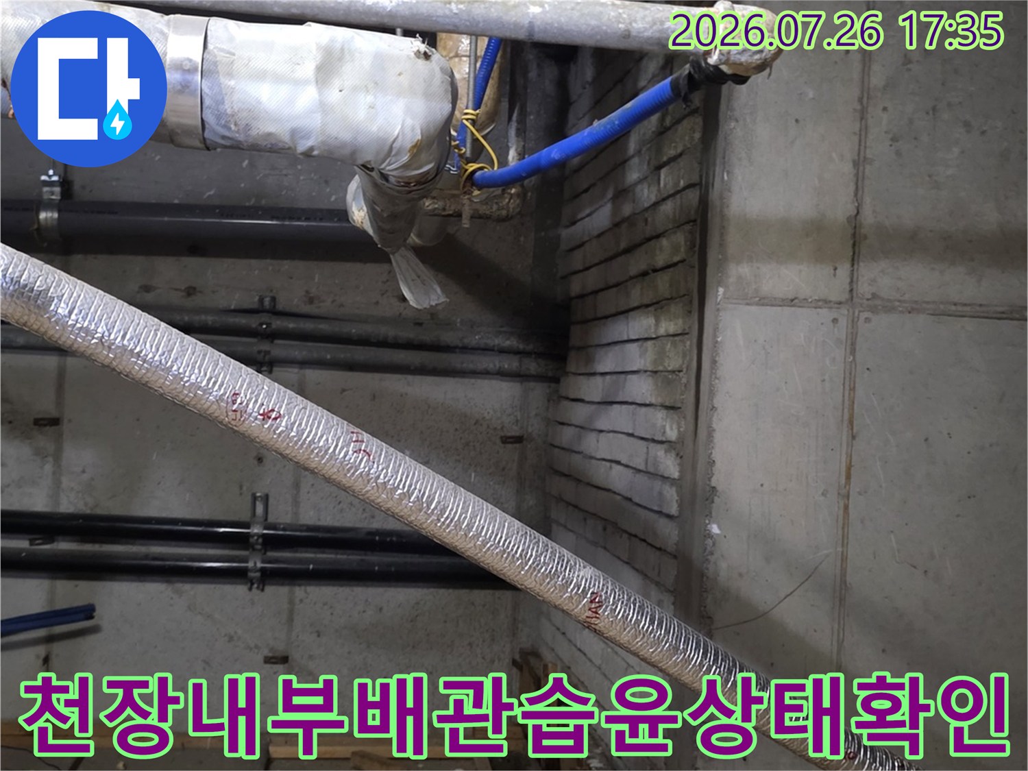 천장 속-은색 보온재 배관과 파란색 호스가 얽혀 있으며 주변 콘크리트에 습기가 찬 모습