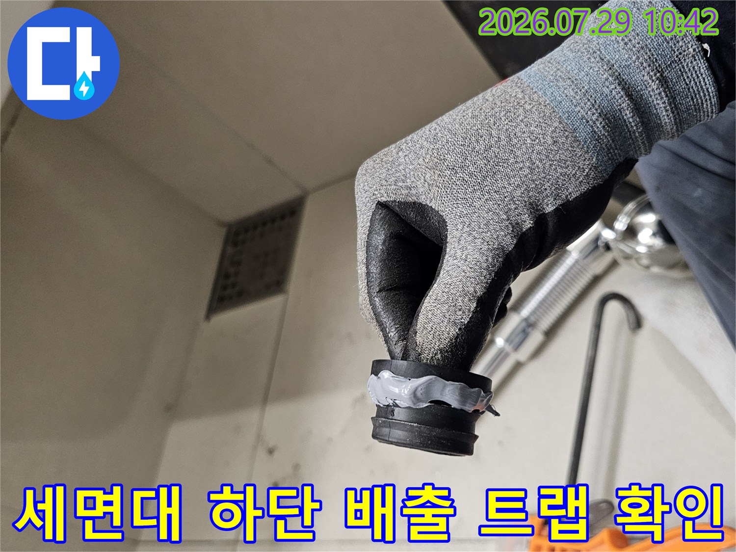 작업자가 보호 장갑을 끼고 세면대 아래쪽 트랩 연결 부위를 점검하는 장면