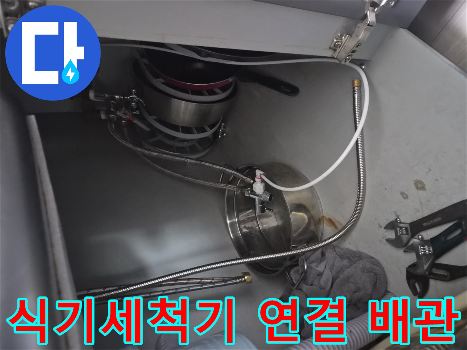 싱크대 하단 식기세척기 급수 호스와 은색 메탈 부품의 모습