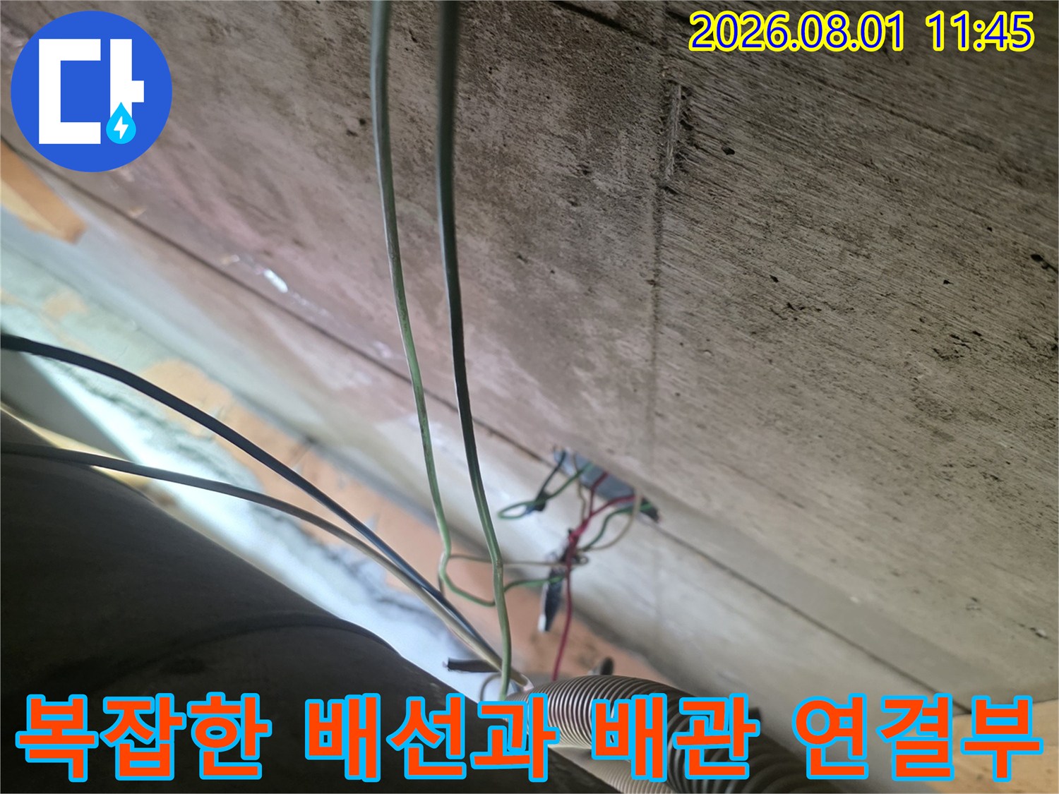 어두운 천장 내부 공간에서 노출된 전선들과 배관이 교차하는 지점의 모습