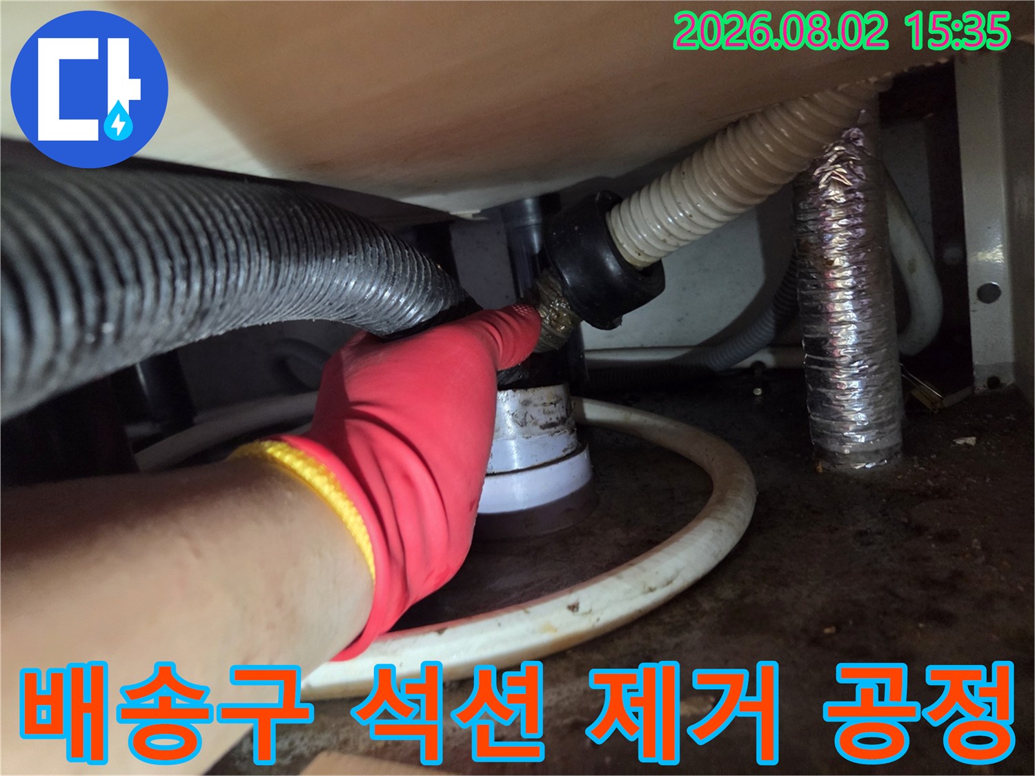 빨간 장갑과 노란색 밴드 세트의 작업자가 싱크대 하부 배관에 석션 호스를 삽입하여 내부 이물질을 청소하는 장면.