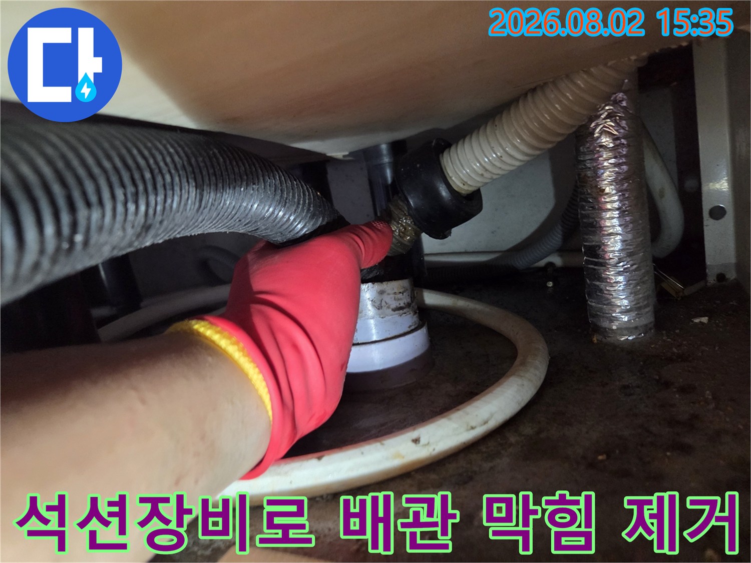 빨간 장갑을 낀 작업자가 석션기를 사용하여 싱크대 하부 배관 내 이물질을 흡입하는 모습