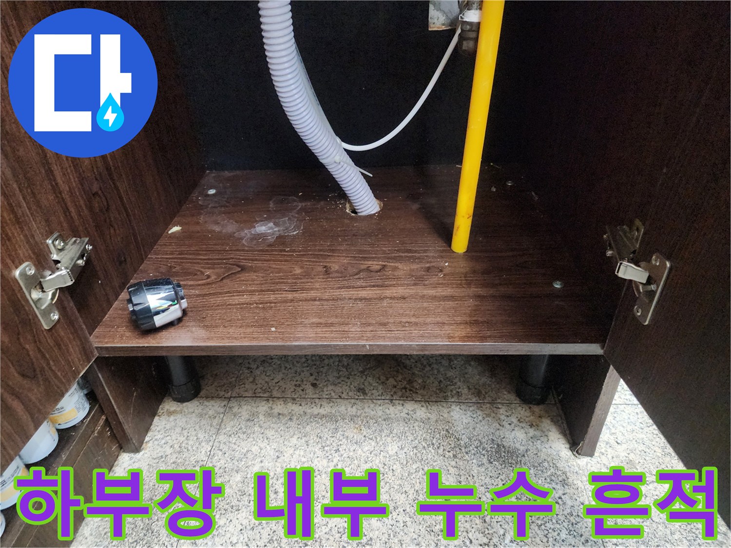 물기가 스며든 싱크대 하단 목재 판넬과 노란색 배관 라인