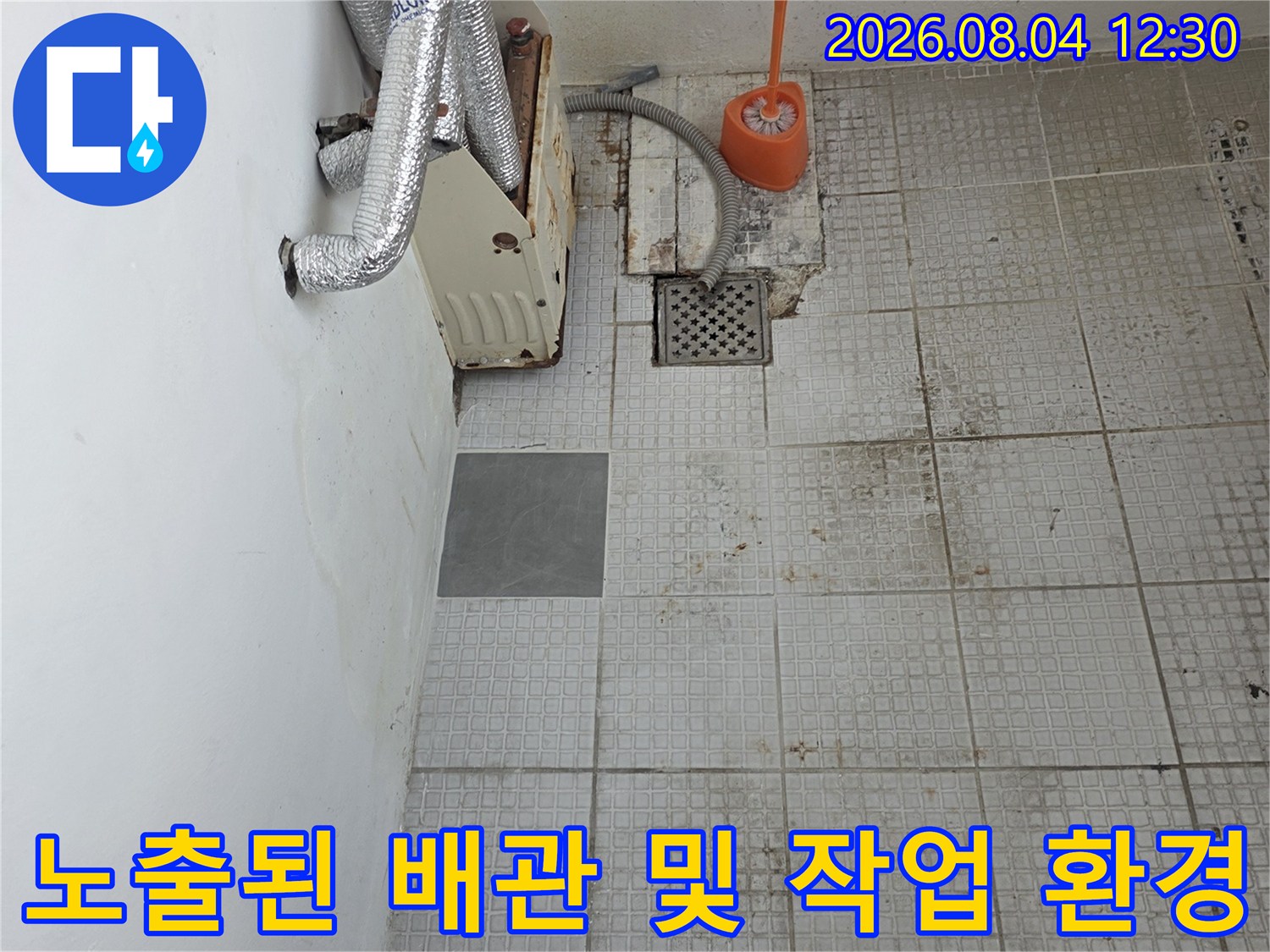 파손된 타일 구간 내 노출된 온수 배관과 수리용 공구