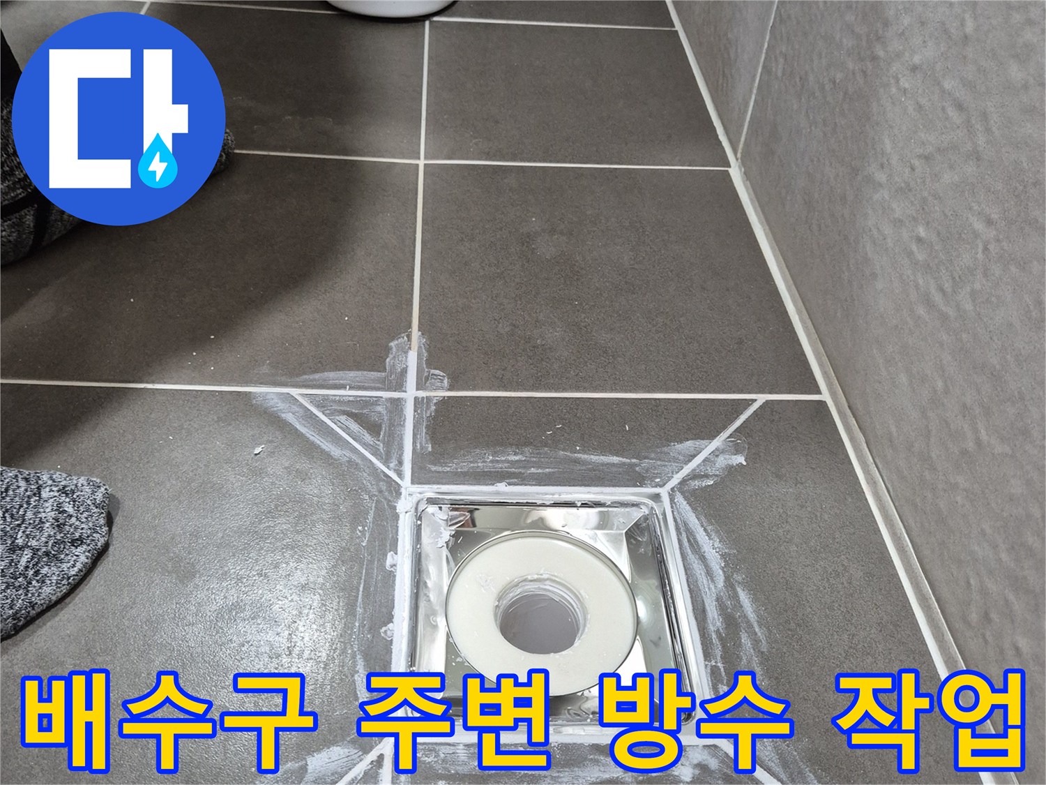 욕실 배수구-주변 타일 틈새에 흰색 방수재를 도포한 모습