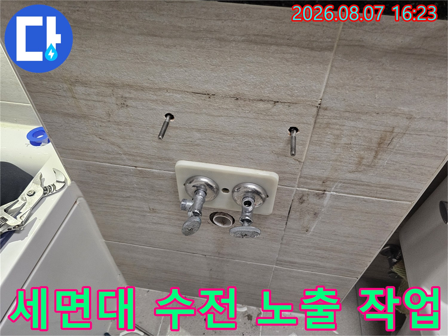타일을 제거하여 드러난 세면대 벽면 수전과 배관 사진입니다.