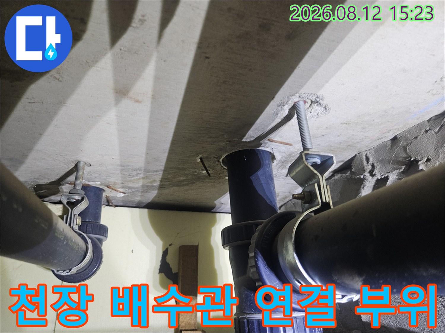 콘크리트 천장에 고정된 검은색 플라스틱 배수관과 금속 지지대의 근접 사진