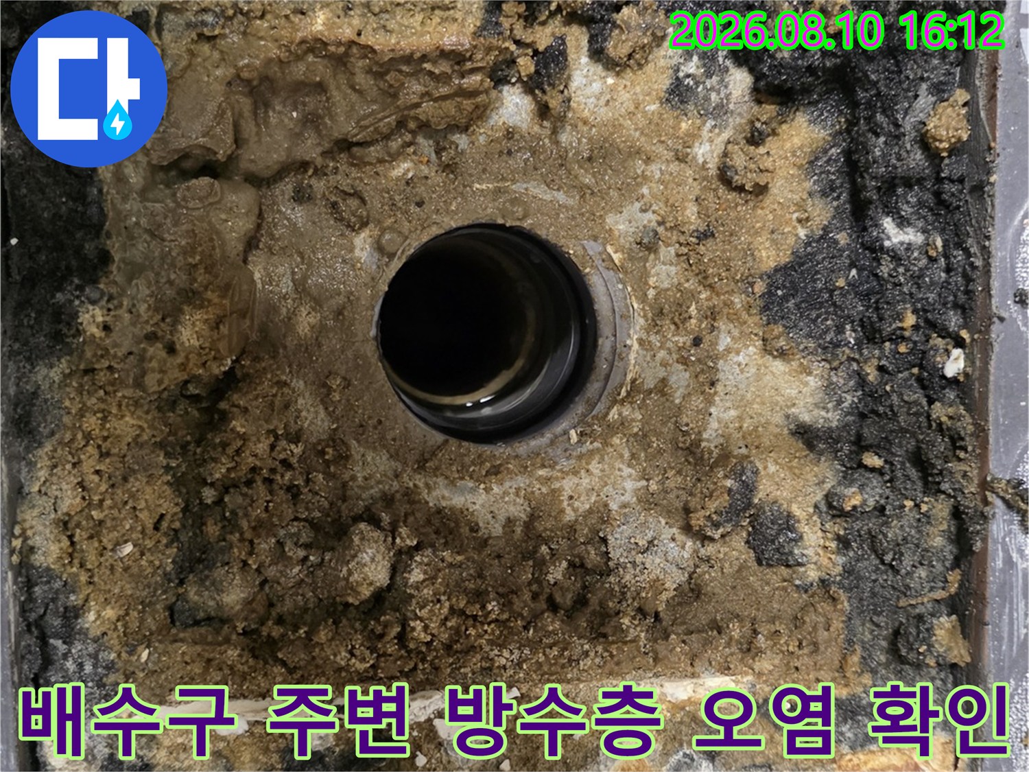 배수구 배관 주위의 젖은 방수층과 이물질이 섞인 현장 사진입니다.
