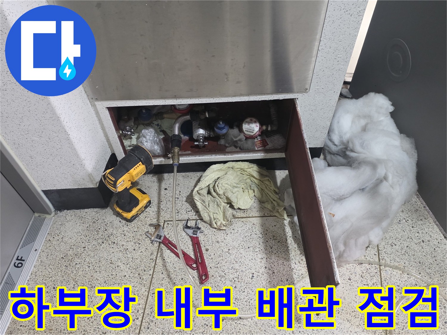 싱크대 하부장 내부의 배관 연결 부위와 전동 드릴 및 공구가 놓여 있는 모습