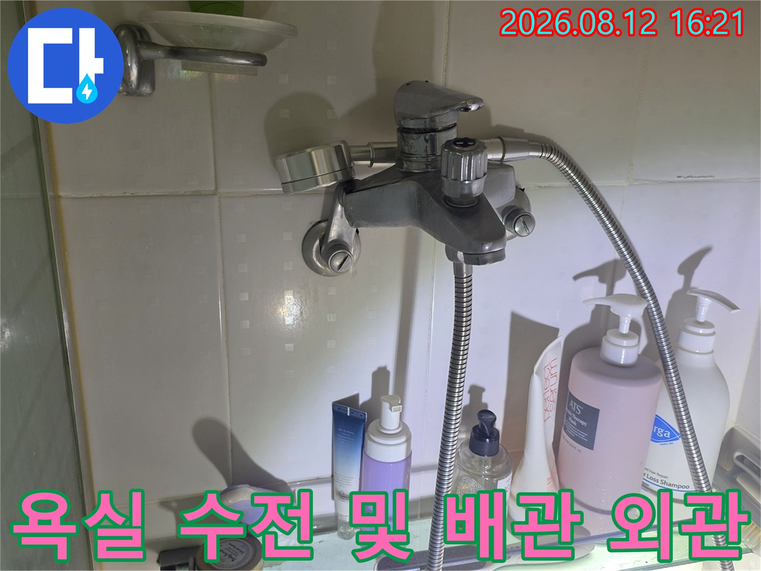 금속 재질의 욕실 샤워 수전과 그 하단의 선반에 놓인 세면도구들