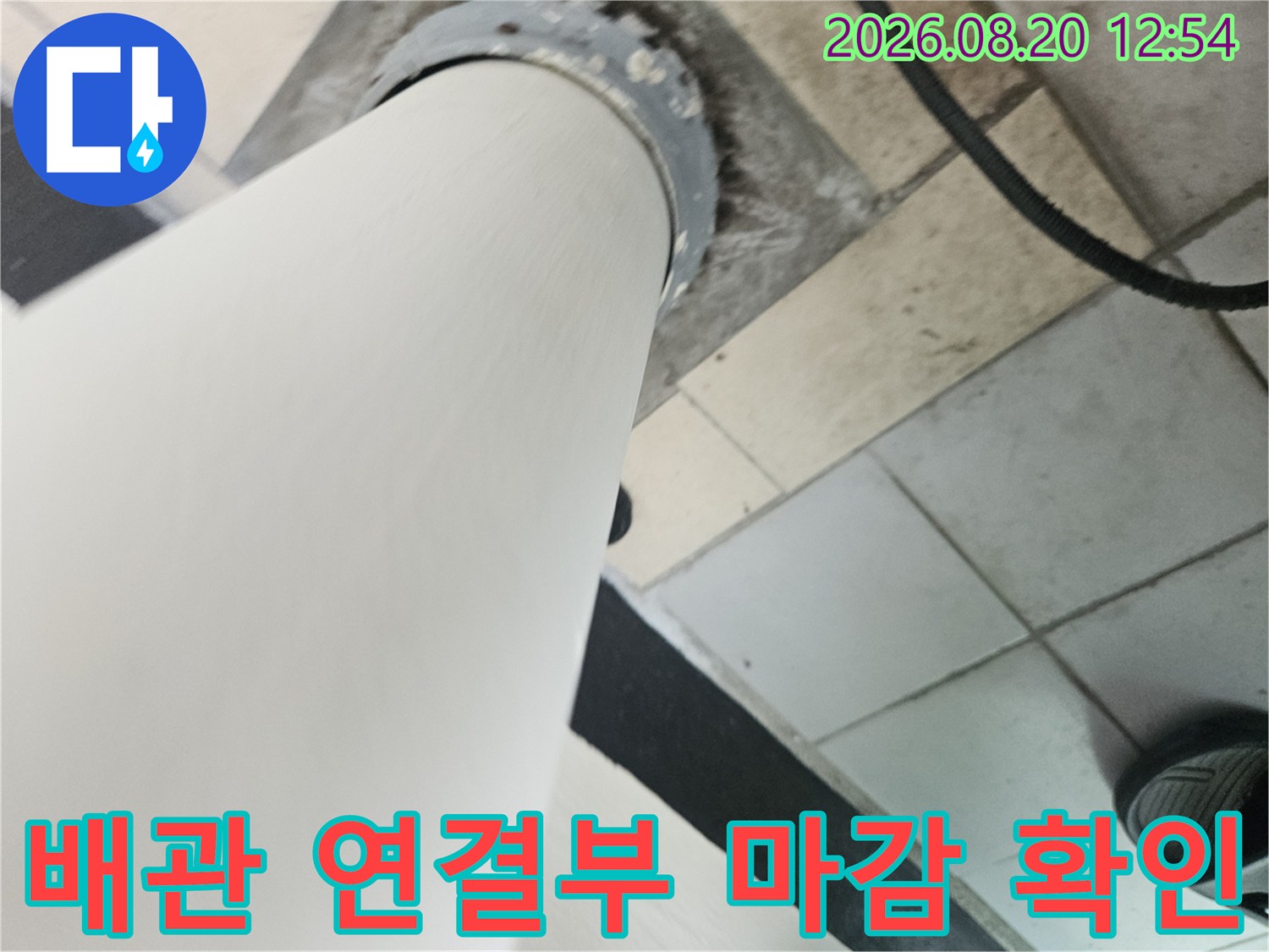 하얀색 우수관과 타일 바닥 사이의 배관 고정 부위 사진입니다.