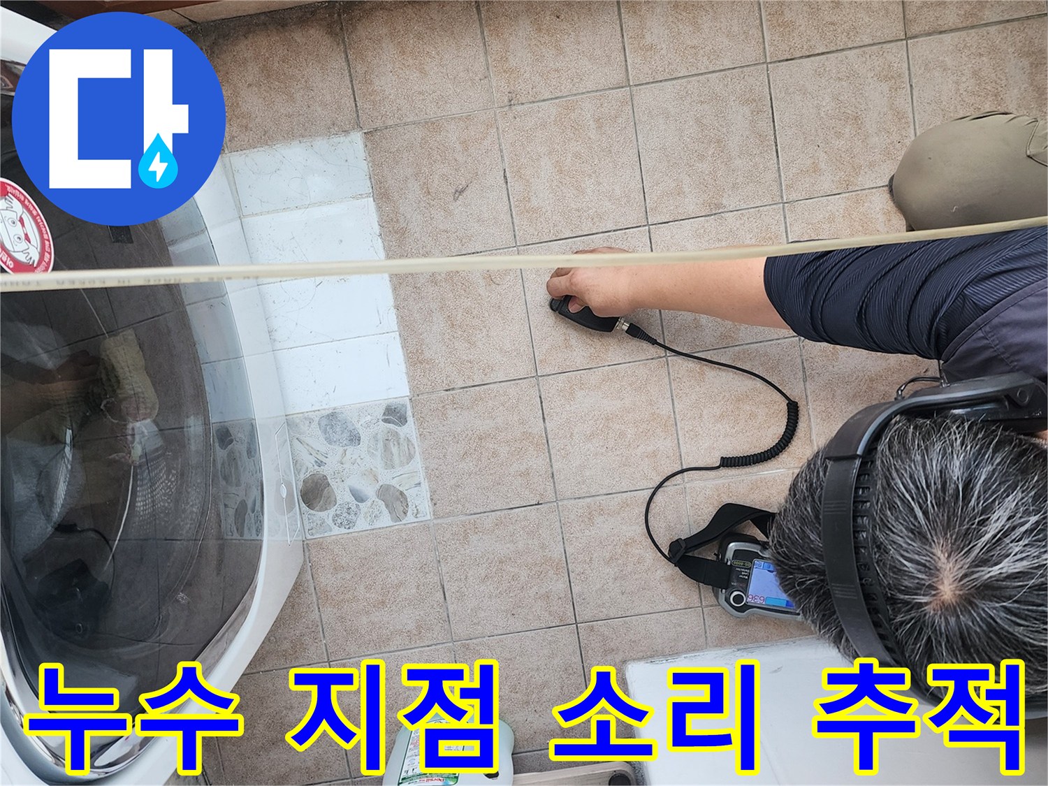 세탁기 옆 바닥 타일에서 청음식 탐지기로 물샘 부위를 찾는 중