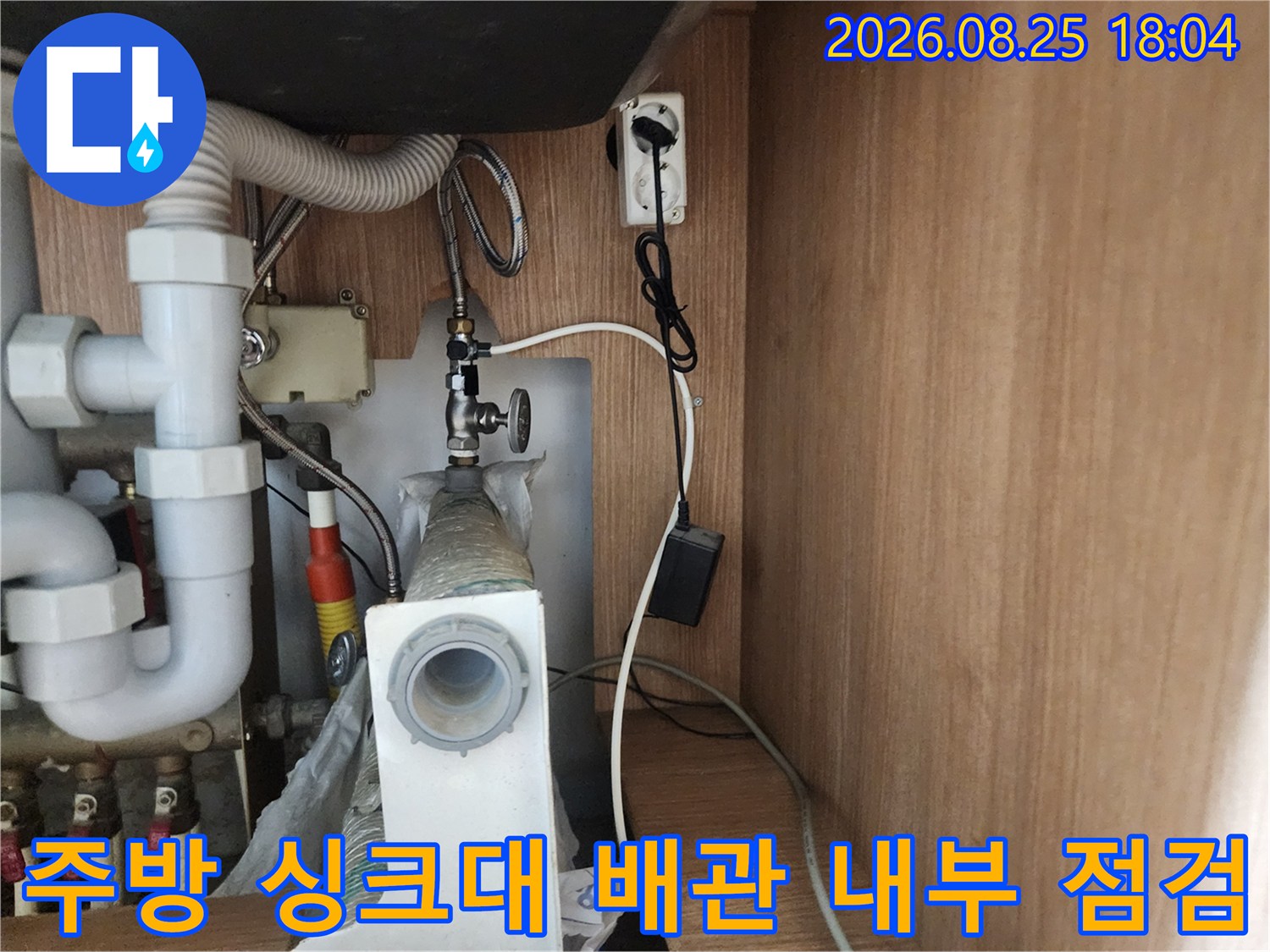 싱크대 하부장 내부에 노출된 급수 밸브와 주름진 배수 호스의 모습입니다.
