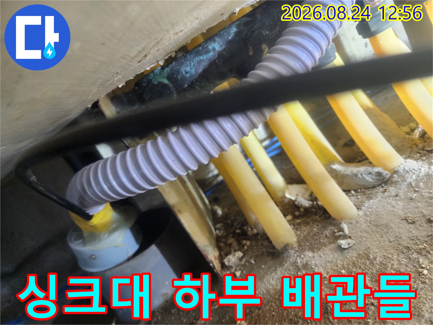 노란색 호스와 흰색 주름관이 얽힌 싱크대 하단 배관 구조