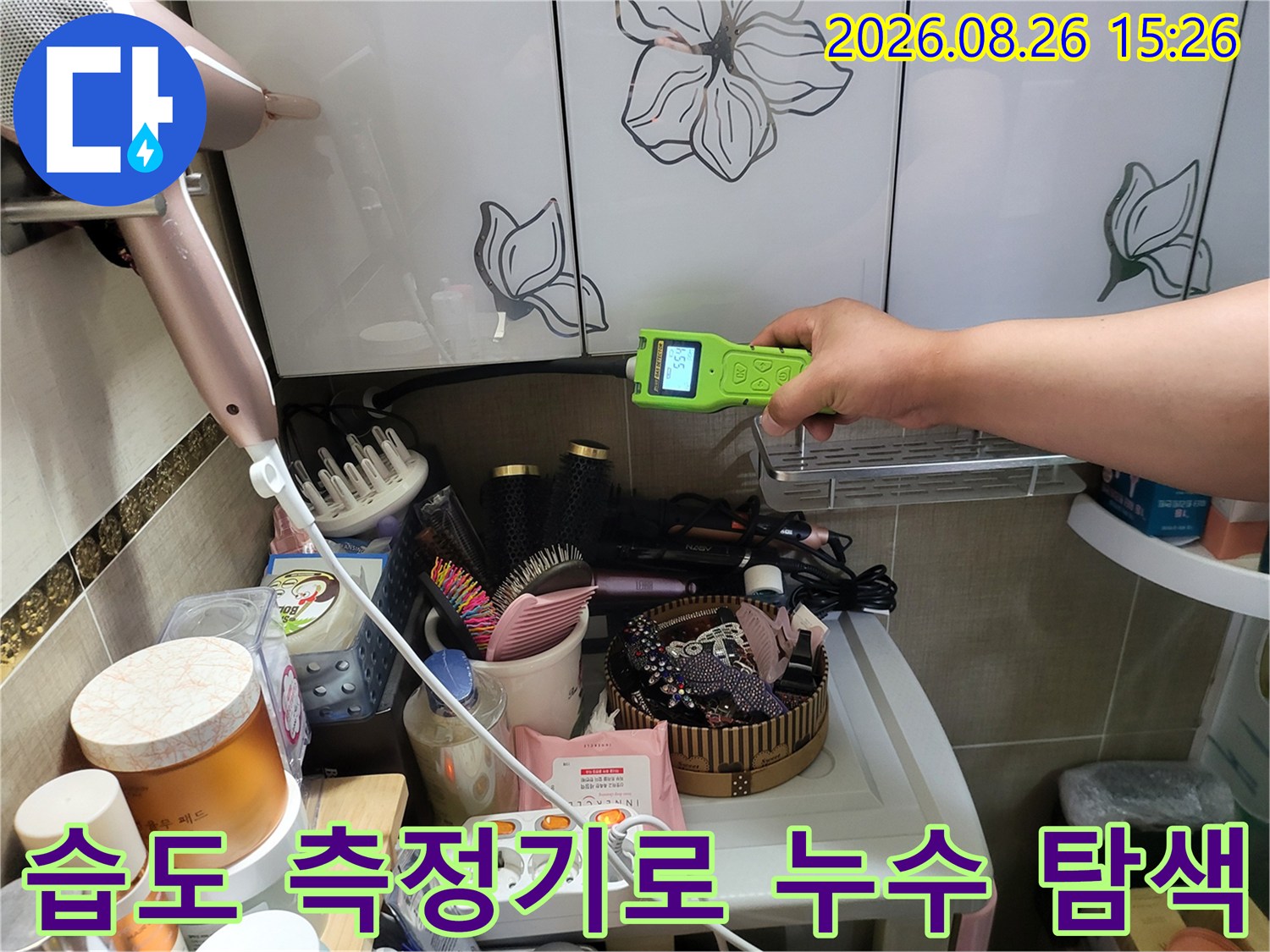 화장실 선반 밑 공간에서 가스식 측정기를 사용하여 습도를 점검하는 모습입니다.