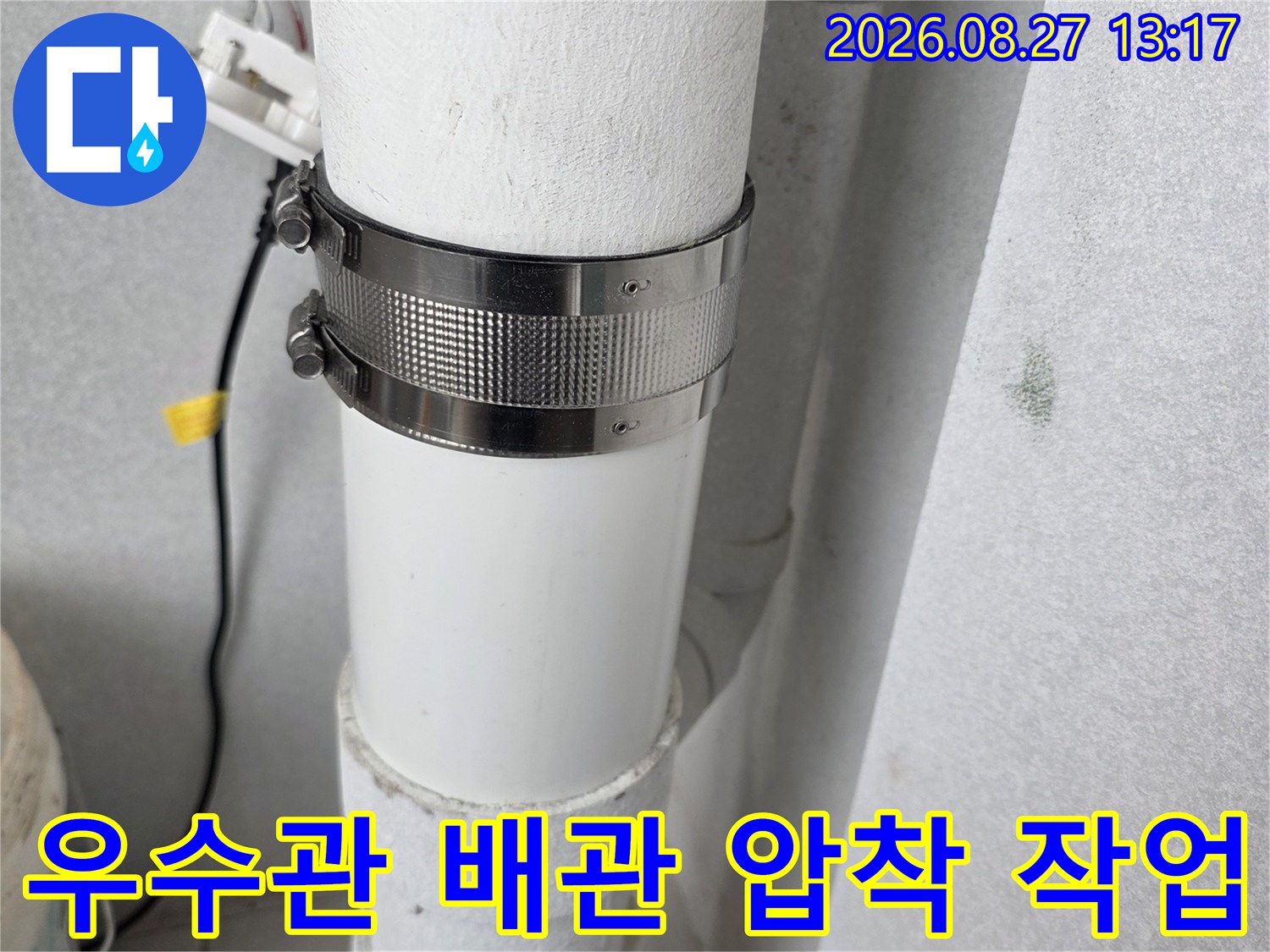 하얀색 우수관 연결 부위에 금속 밴드를 채워 고정하는 모습입니다.