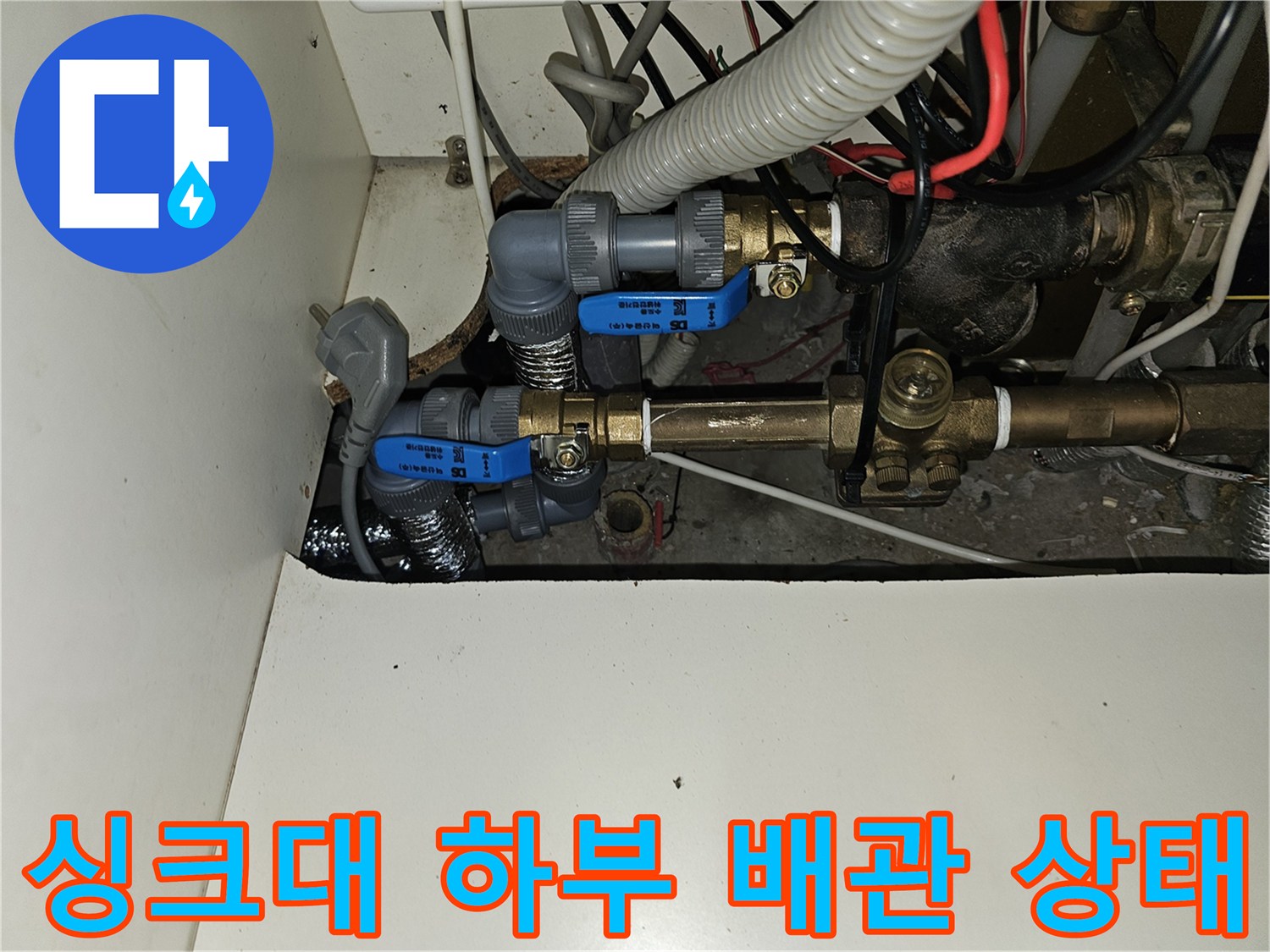 주방 싱크대 아래 공간에 복잡하게 얽힌 난방 분배기 및 보온재 배관
