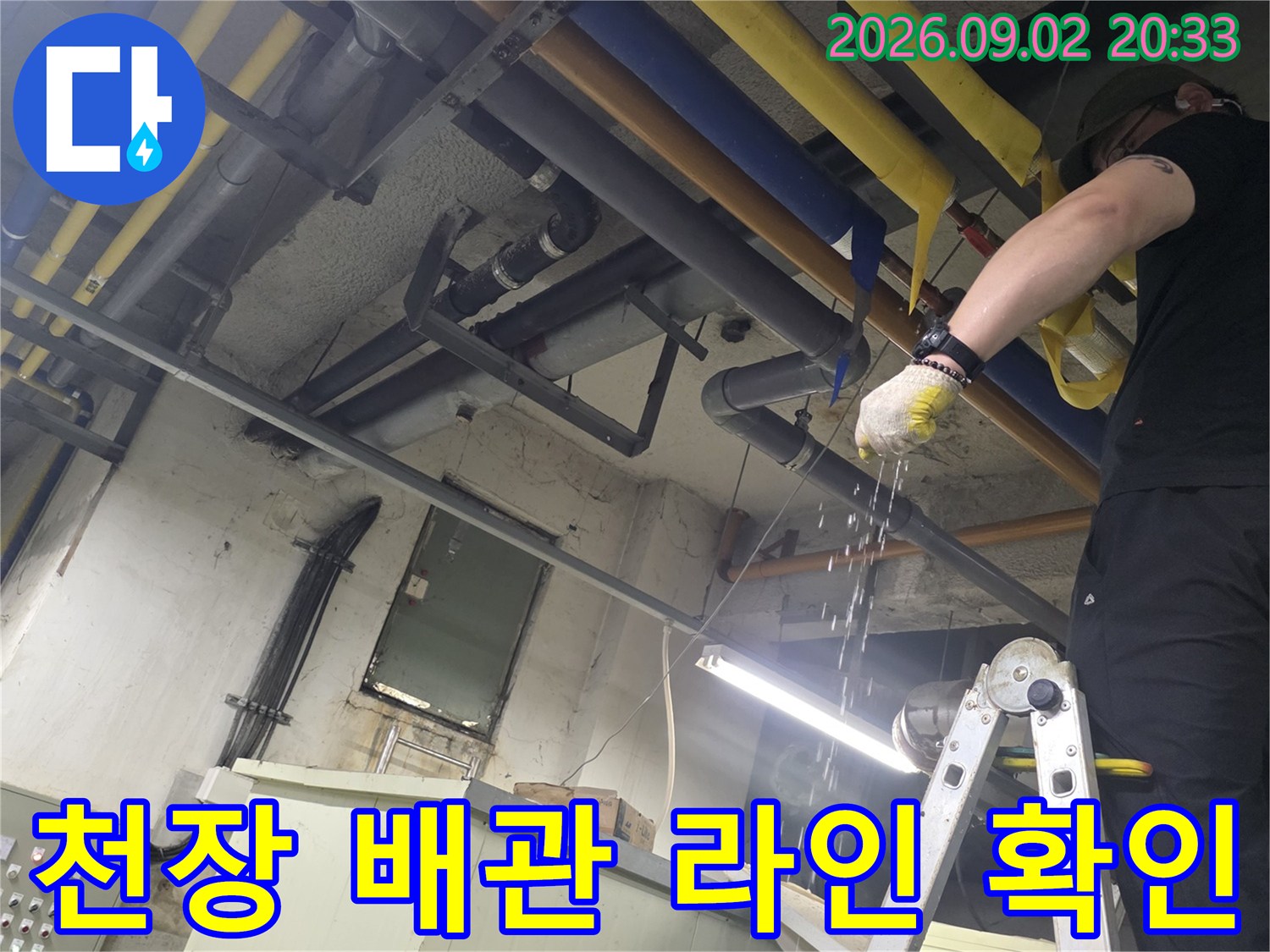 사다리 위에서 작업자가 천장 배관의 연결 상태를 세밀하게 관찰하고 있습니다.