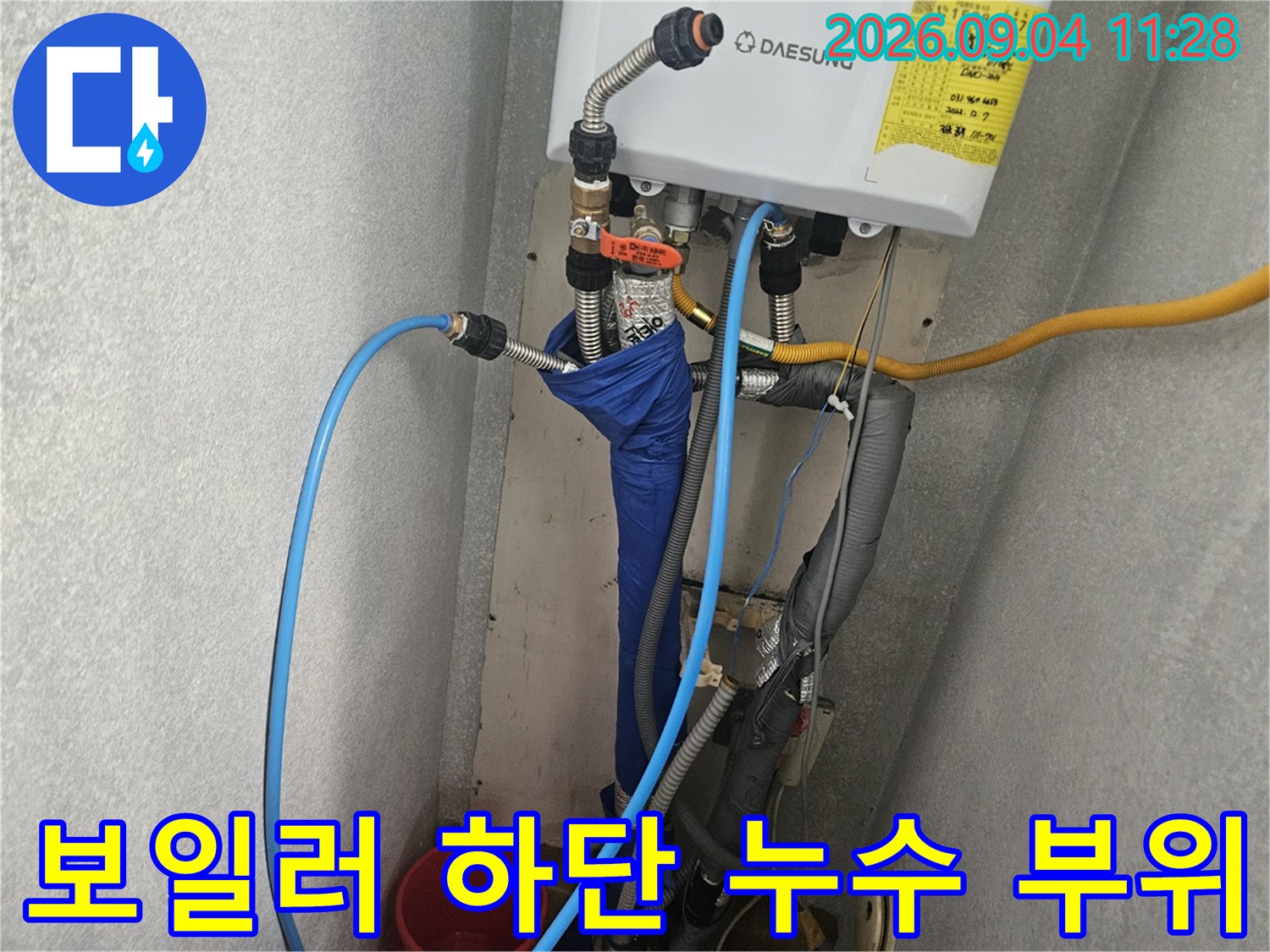 보일러 아래쪽의 급수 및 온수 배관 연결 상태를 점검하는 사진입니다.