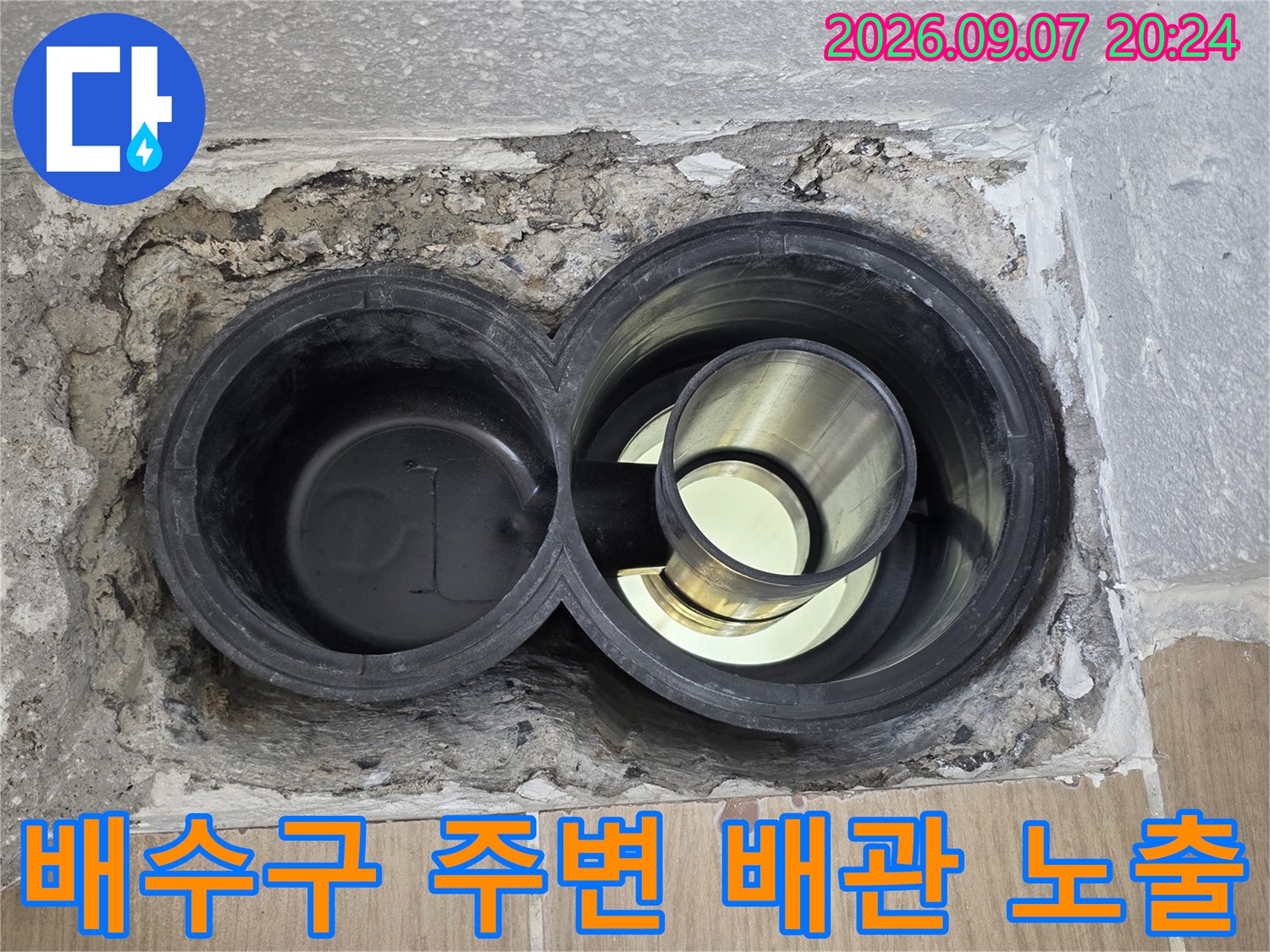 노출된 욕실 배수관과 그 주변의 불완전한 마감재 상태를 보여줍니다.