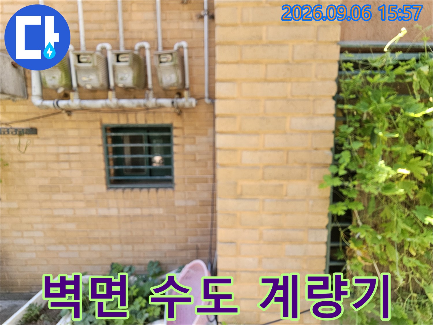벽돌 벽에 고정된 수도 계량기와 배관 모습입니다.